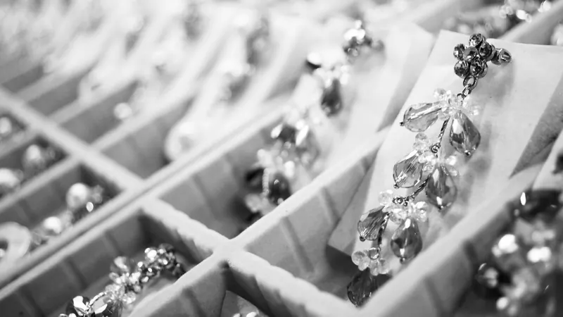 Black-and-white photo of crystal earrings arranged in a compartment display tray, showing different types of earring backs