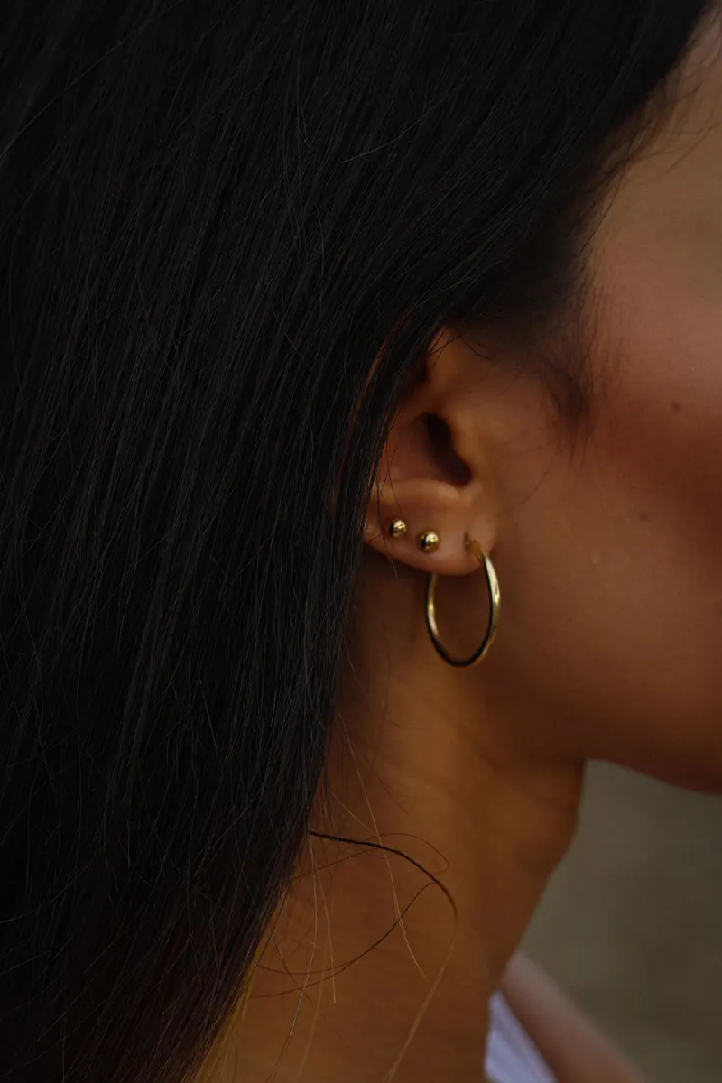 Ear with a curated stack of small studs and a thin gold hoop in the lobe, showing what gauge regular earrings use