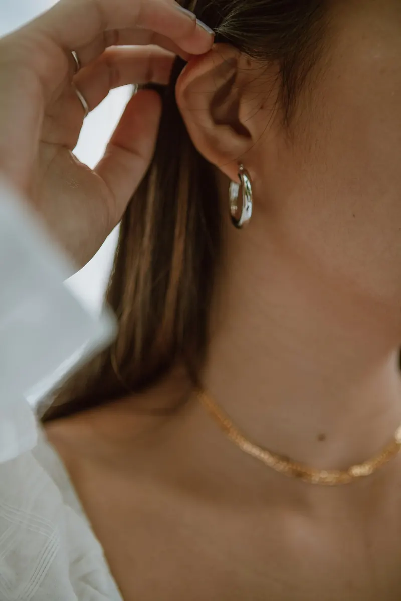 Woman tucking her hair behind her ear with a small silver hoop visible, a simple look that works for helix earrings